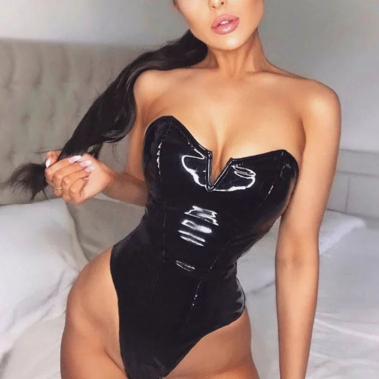 Kobieta w czarnym, lakierowanym body na tle jasnego łóżka i ściany