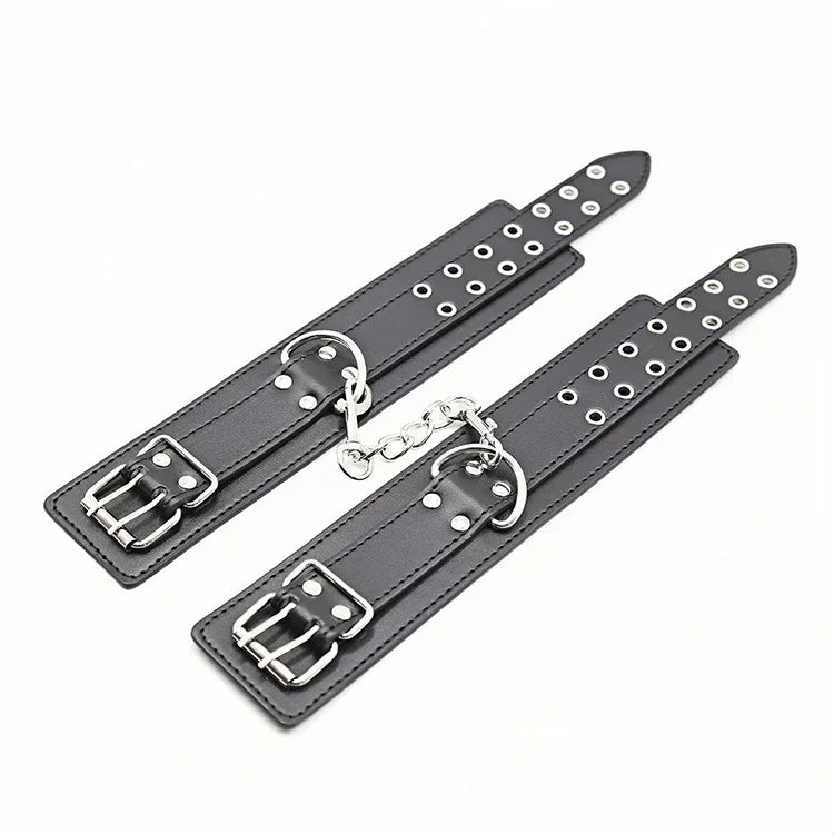 Czarne skórzane kajdanki z metalowymi sprzączkami, oczkami i łańcuszkiem na białym tle